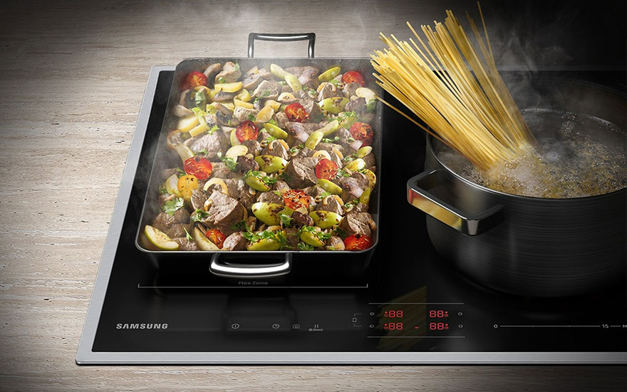 Een zwarte kookplaat met een braadpan gevuld met vlees en groenten, naast een pot kokende spaghetti.