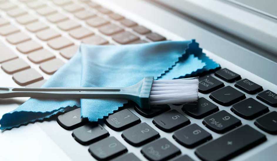 Un clavier d'ordinateur portable blanc et noir est en cours de nettoyage avec un chiffon bleu et une brosse blanche.