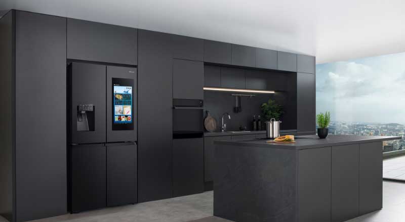 Een moderne donkere keuken met strak design, kookeiland en slimme koelkast met ingebouwd scherm en waterdispenser.