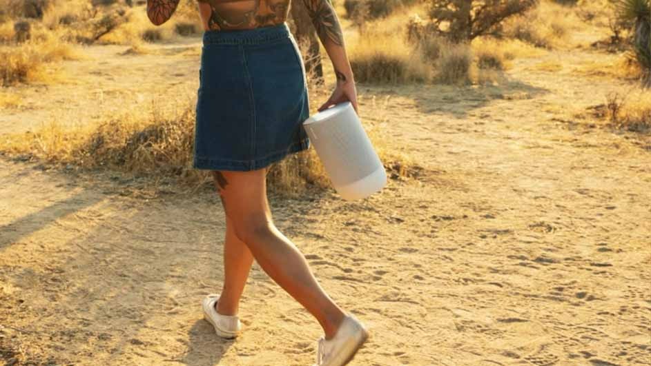 Une jupe en jean bleue et un haut tatoué tenant un cylindre blanc sur un sentier de terre avec de l'herbe sèche.