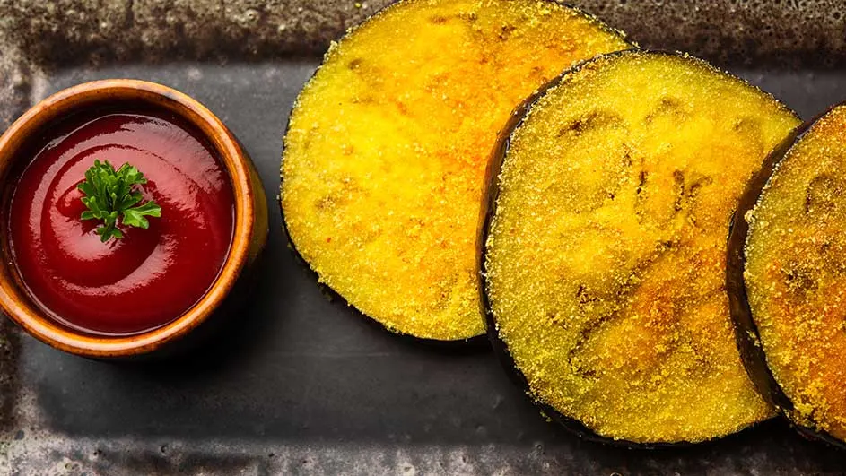 Tranches d'aubergine frites, sauce tomate dans un bol en bois, sur une assiette sombre. Persil sur la sauce.