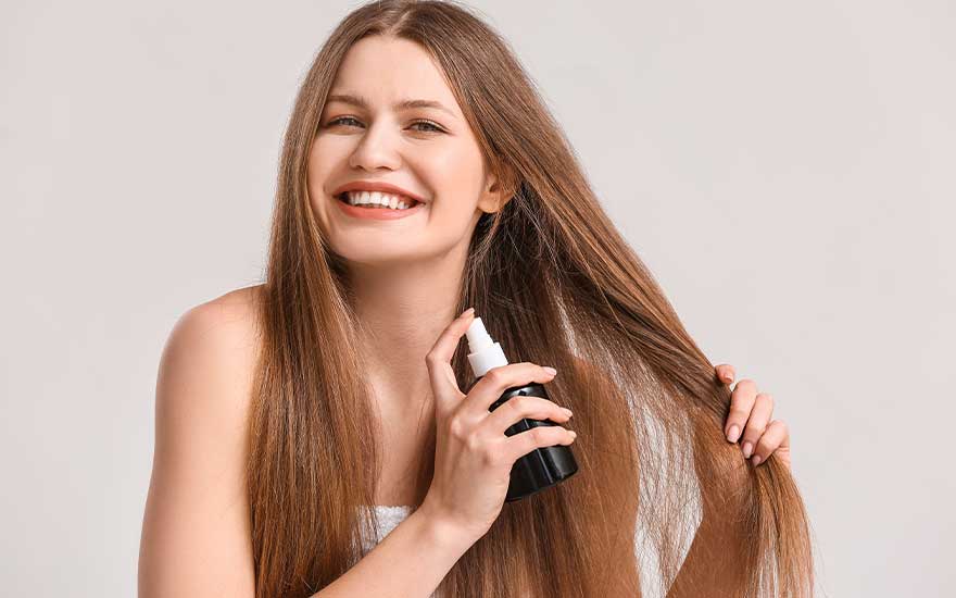 Une bouteille noire et blanche est tenue près de longs cheveux châtains devant un fond clair.