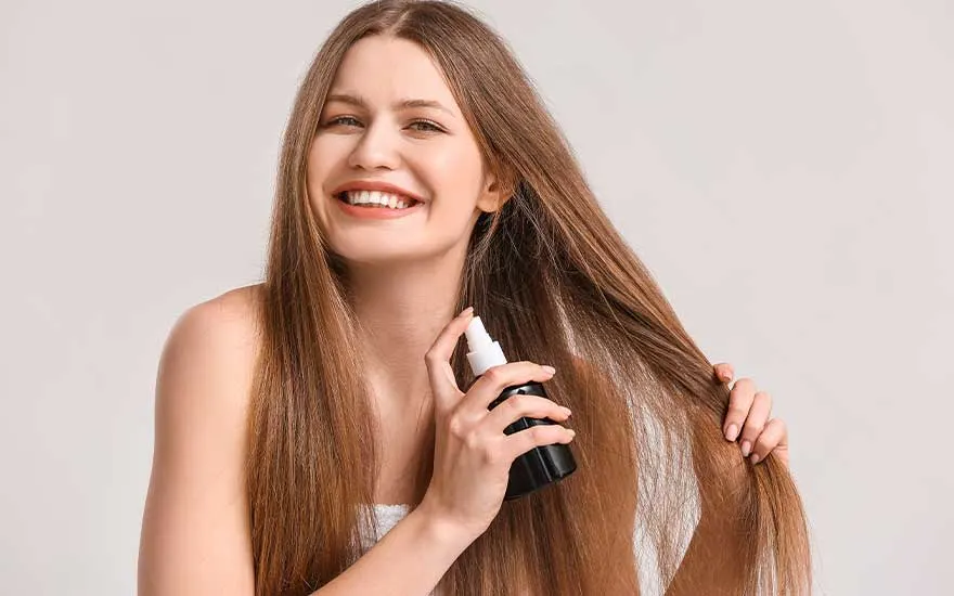 Une bouteille noire et blanche est tenue près de longs cheveux châtains devant un fond clair.