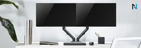 Deux écrans noirs sur un bureau blanc avec clavier, souris, et pot à crayons. Plante verte à gauche.