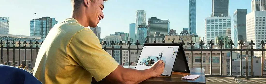 Un ordinateur portable est posé sur une table, avec une ville en arrière-plan et une clôture en métal au milieu.