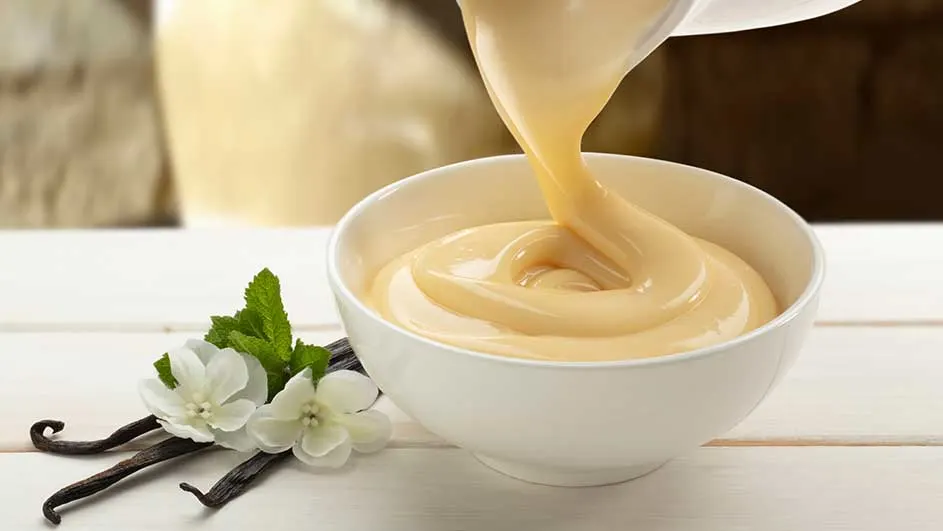 Een witte kom wordt gevuld met gele vloeistof, met vanille en munt op een witte houten tafel.