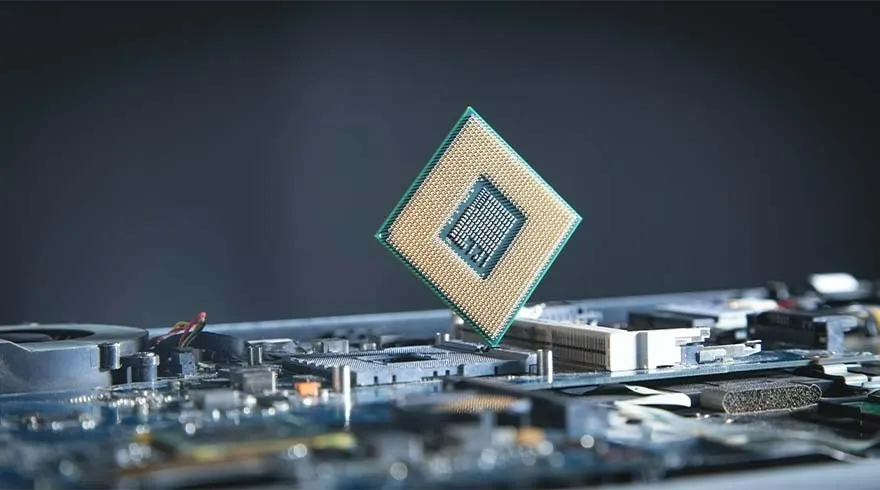 Een computerprocessor met gouden rand zweeft boven een moederbord met diverse elektronische componenten tegen een donkere achtergrond.