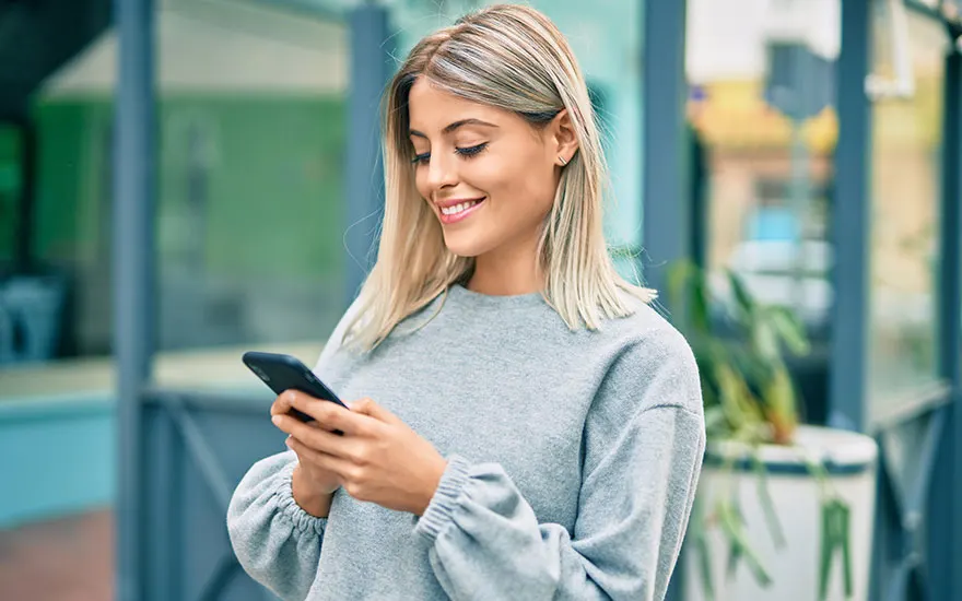 Une personne utilise un smartphone devant une fenêtre. Une plante est visible en arrière-plan.