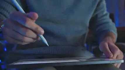 Een hand houdt een witte stylus boven een tablet. De achtergrond is wazig en blauw getint.