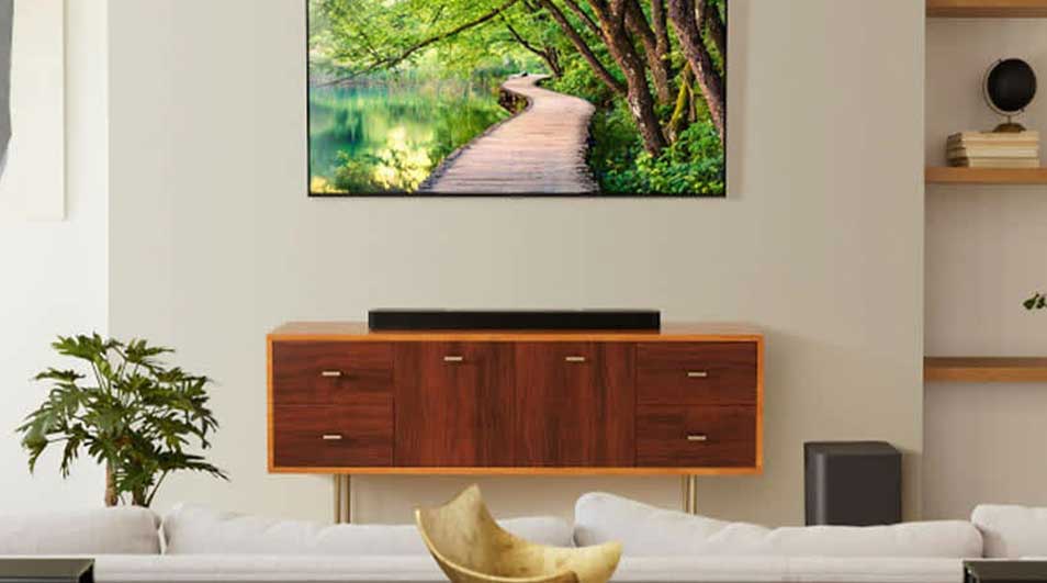 Salon avec une TV montrant un chemin boisé. Un meuble bas en bois supporte une barre de son. Un canapé blanc est devant.