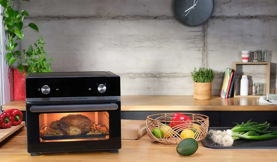 Four avec poulet rôti, légumes, fruits et herbes sur un comptoir en bois devant un mur gris.