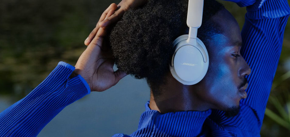 Un homme porte un pull bleu et un casque blanc. Il ajuste le casque avec sa main.