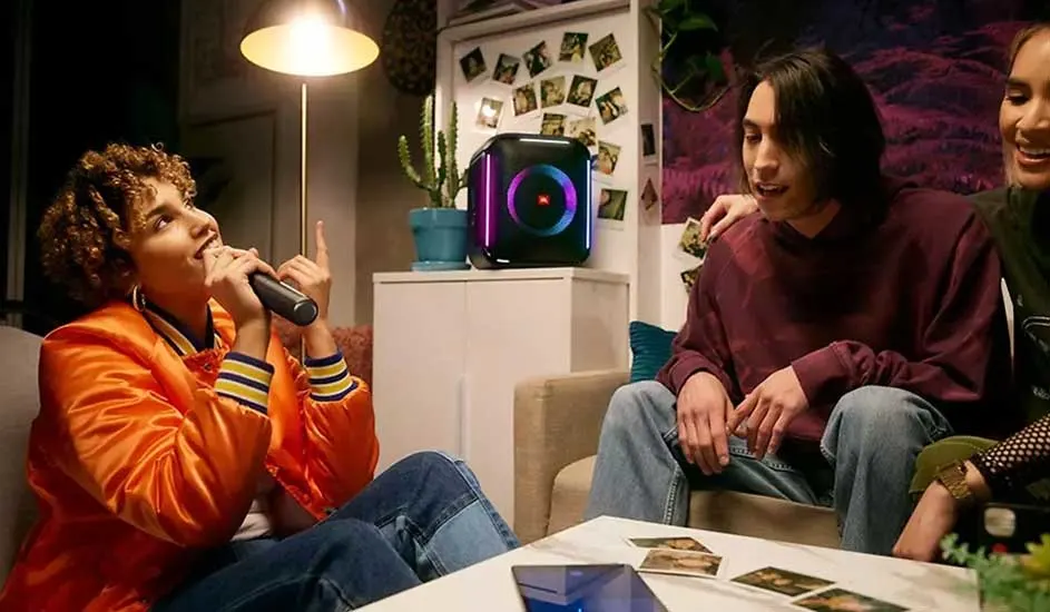 Un groupe dans un salon avec une enceinte lumineuse sur une armoire blanche, un microphone et une tablette sur une table.