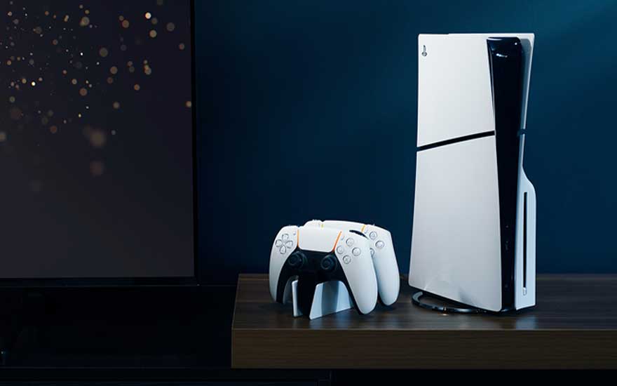 Een moderne gaming setup met een witte PlayStation 5-console, twee wireless controllers en een zwart dockingstation, geplaatst op een houten bureau tegen een donkerblauwe achtergrond.