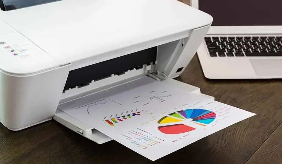 Een witte printer print een blad met een gekleurde cirkeldiagram en staafdiagram, naast een laptop op een houten bureau.