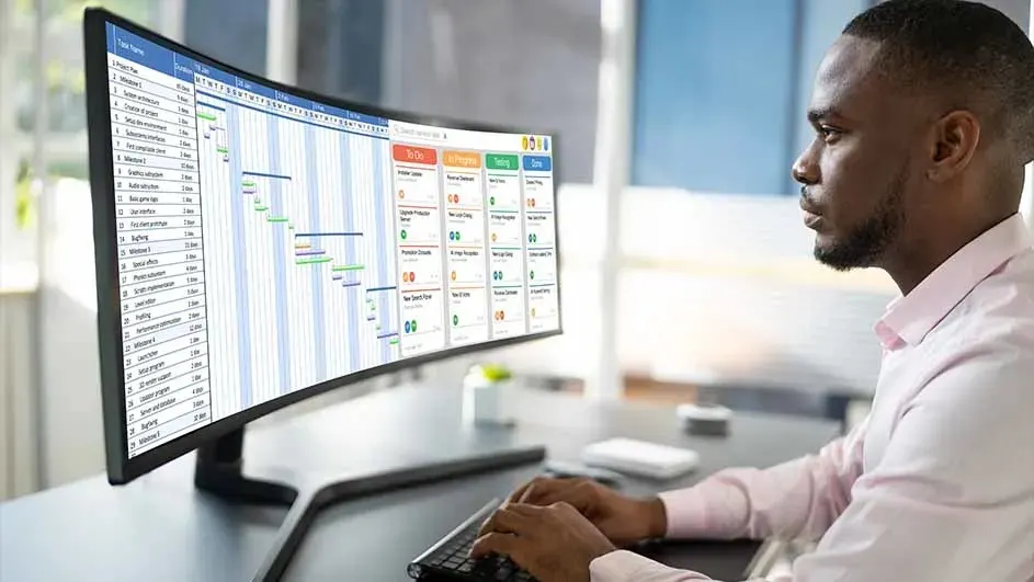 Un écran large affiche un tableau de planification. Un clavier est devant l'écran sur un bureau.