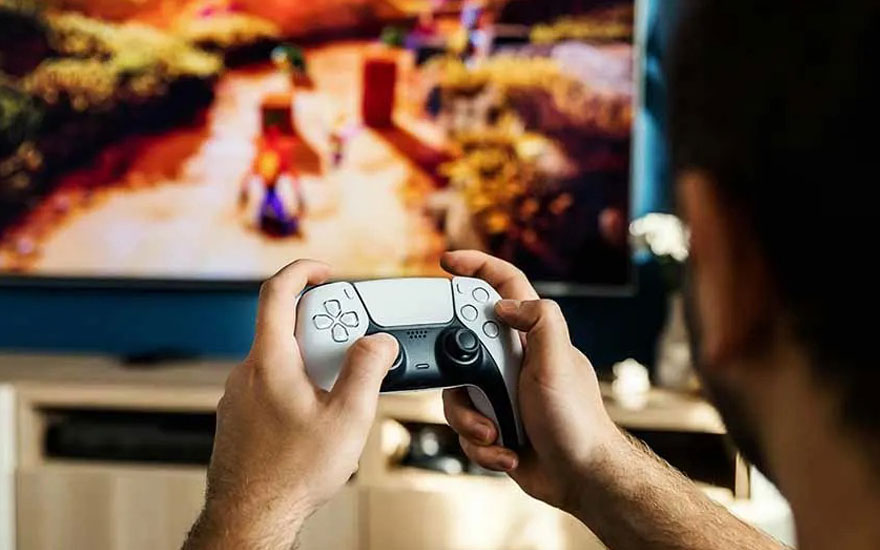 A person is playing a colourful game on a PS5 using a white DualSense controller, facing a large television in a living room.