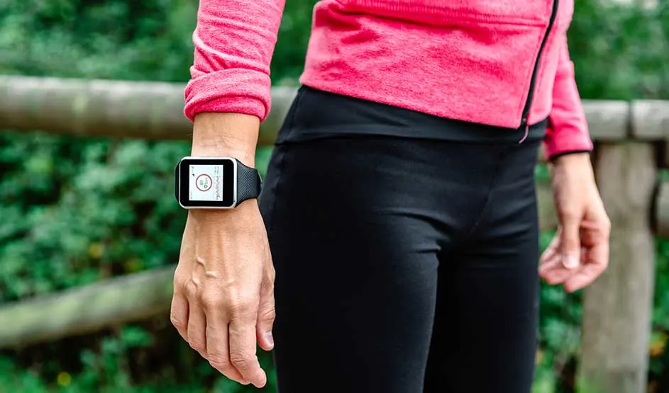 Een sportieve persoon draagt buiten een smartwatch met gezondheidsgegevens, gekleed in roze top en zwarte legging.