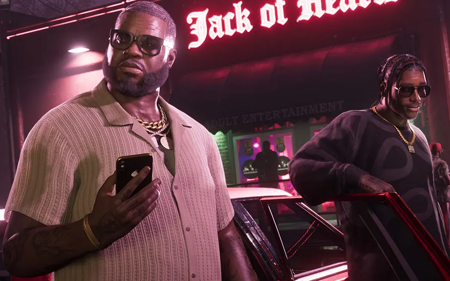 Two men standing at night by a car outside a brightly lit club.