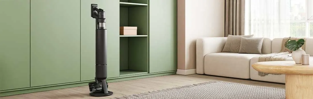 Elegante zwarte steelstofzuiger op rond station voor grote groene kast, in warme woonkamer met beige bank en houten salontafel.