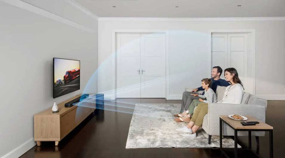 Salon lumineux avec TV, meuble en bois clair, canapé gris, tapis, table. Porte blanche en arrière-plan. Effet sonore visible.