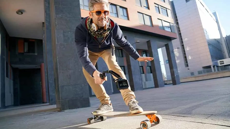Iemand rijdt op een elektrisch skateboard in een moderne stad, houdt een afstandsbediening vast en balanceert met gebogen knieën.