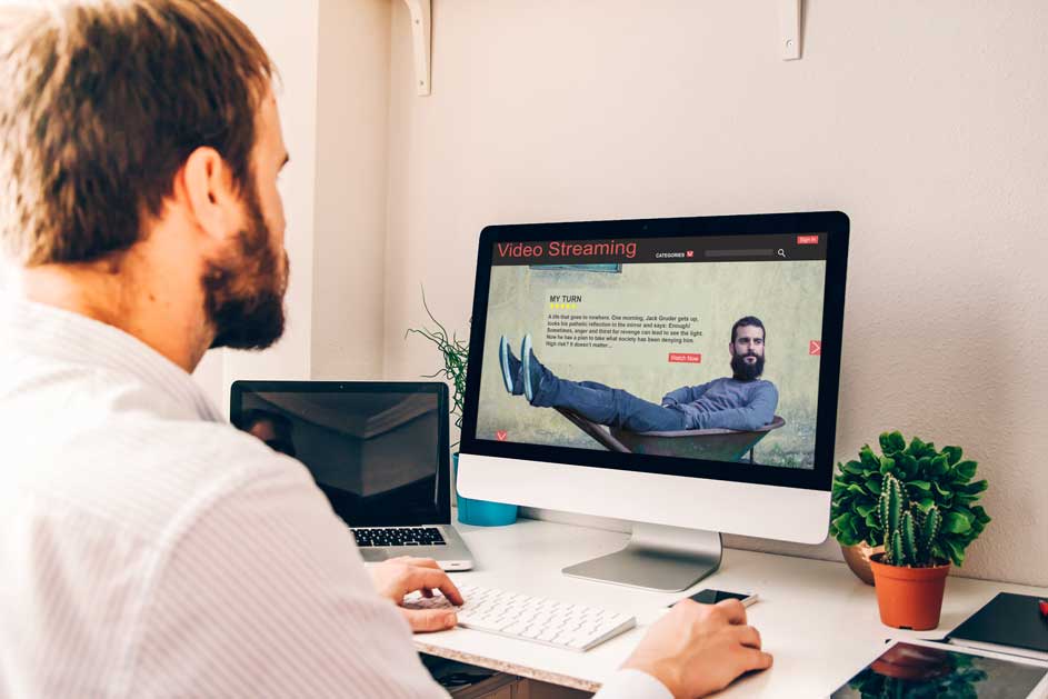 Un homme utilise un ordinateur pour regarder des vidéos en streaming sur un bureau blanc avec des plantes.