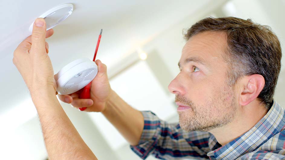 Een witte rookmelder en deksel worden gemonteerd aan een wit plafond met een rode schroevendraaier.