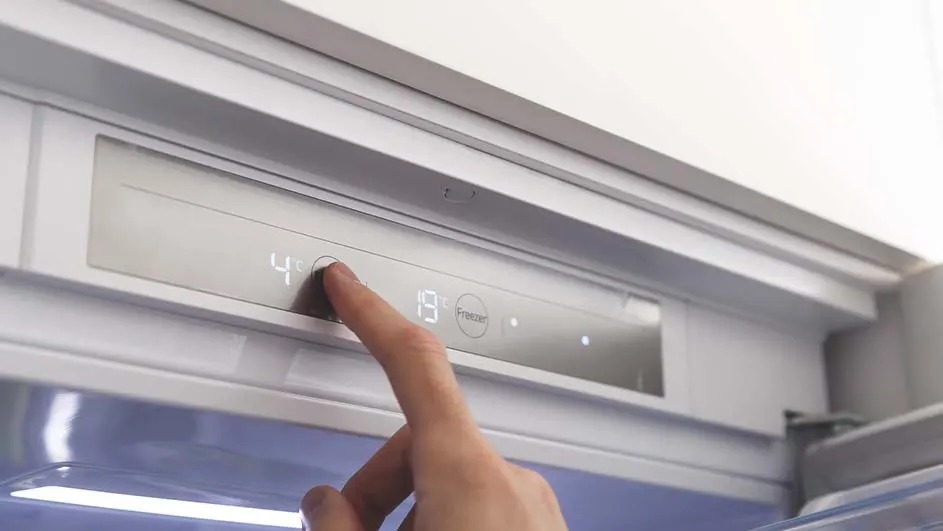 Un doigt appuie sur le bouton "4" sur un panneau gris intégré dans un réfrigérateur blanc. Un autre bouton affiche "19".