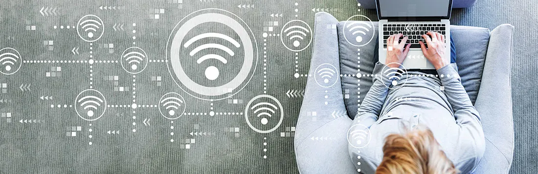 Vue aérienne d'un ordinateur portable sur un canapé gris, avec des symboles WiFi sur un tapis gris.