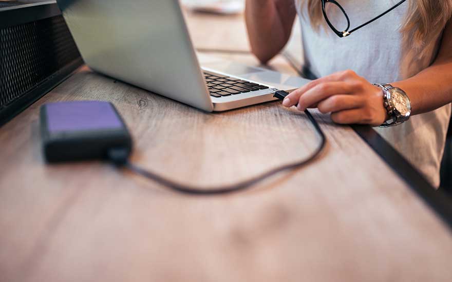 Un ordinateur portable et un disque dur externe sont sur une table en bois. Un câble noir les relie.