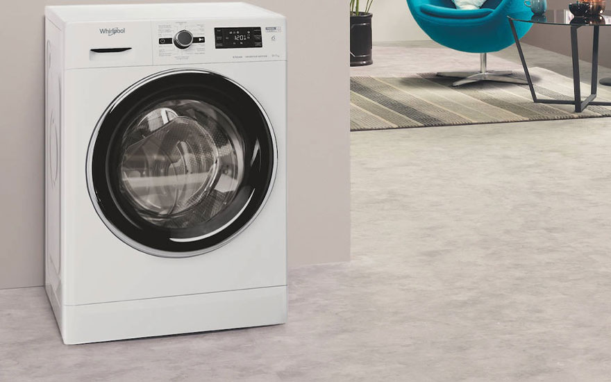 Une machine à laver blanche se trouve dans une pièce avec un fauteuil bleu et un tapis à rayures.