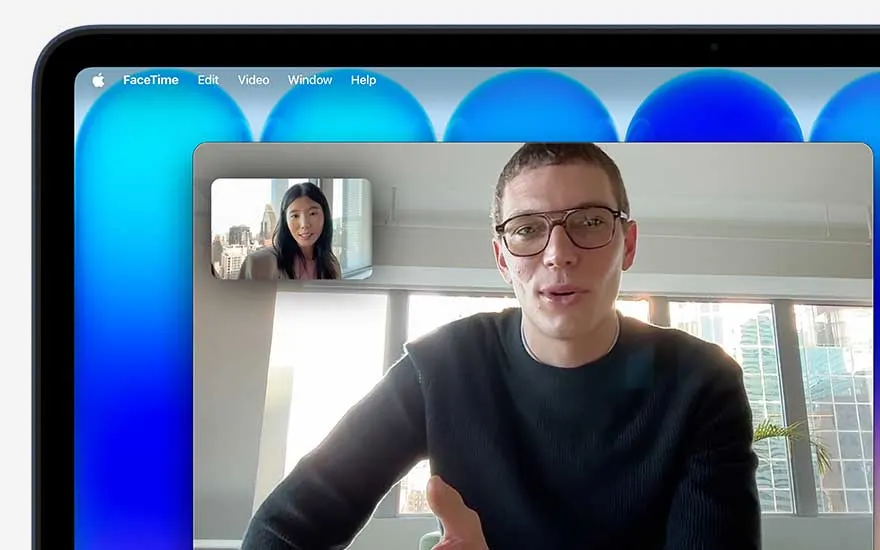 On the MacBook display a FaceTime call is in progress, showing a man in a large window and a woman in a smaller frame with city views.
