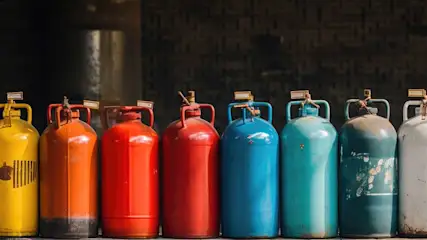 Rangée de bonbonnes de gaz colorées (jaune, orange, rouge, bleu, turquoise, blanc) avec des étiquettes sur un fond sombre.