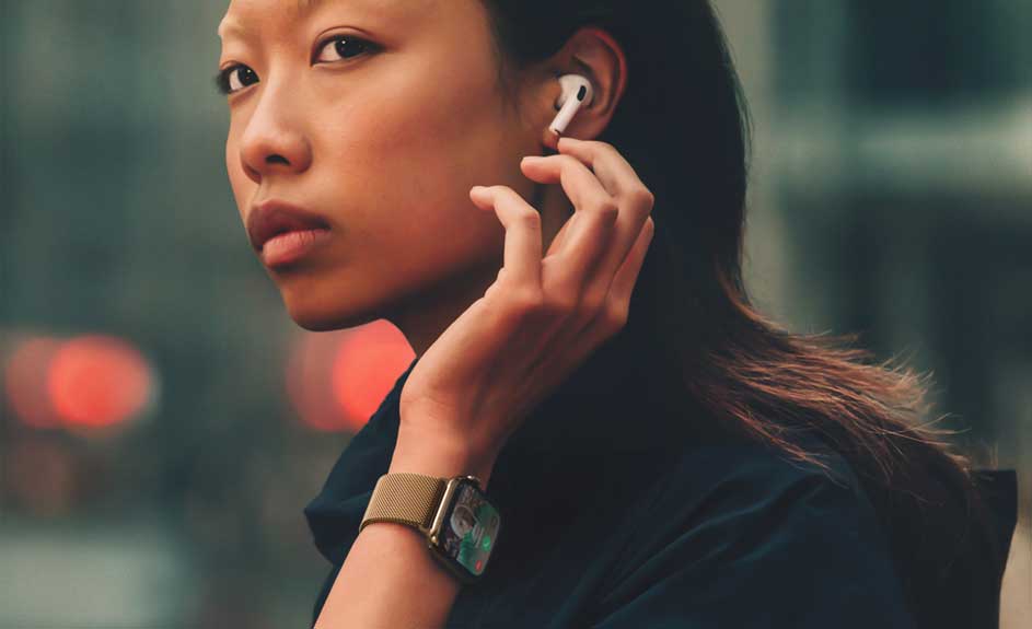 Een close-up van een horloge met een gouden band, een witte oortelefoon en de achtergrond is wazig met rode en groene lichten.