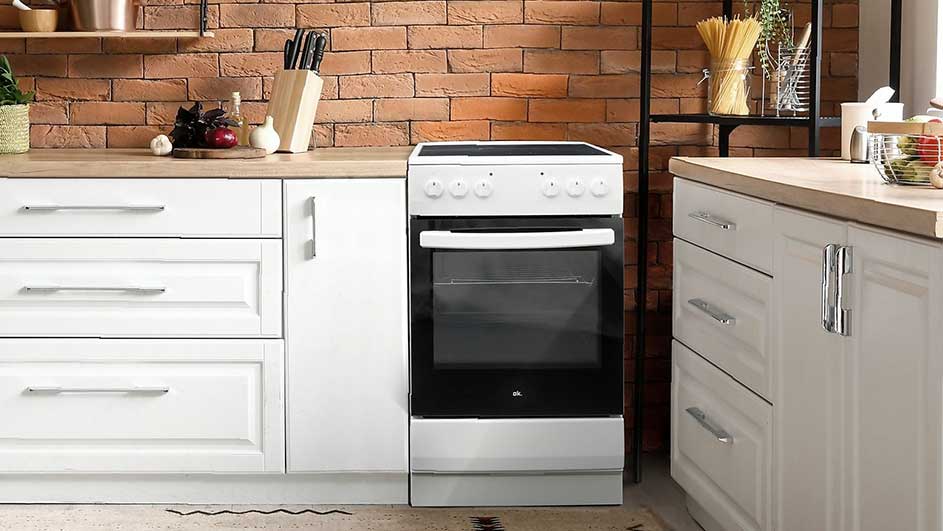 Cuisine avec four blanc entre des armoires blanches sous un plan de travail en bois, mur en briques rouges en arrière-plan.