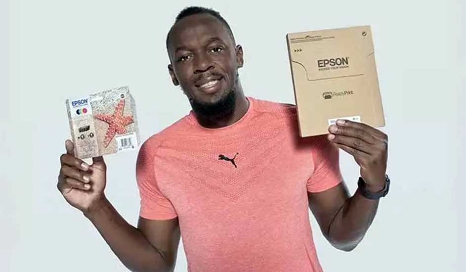 Een persoon in een roze shirt houdt een Epson-fotopapierpakket en een kartonnen doos tegen een witte achtergrond.