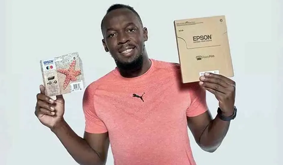 Un homme tient des emballages Epson. Un paquet montre une étoile de mer rouge. Il porte un t-shirt rose Puma sur fond blanc.