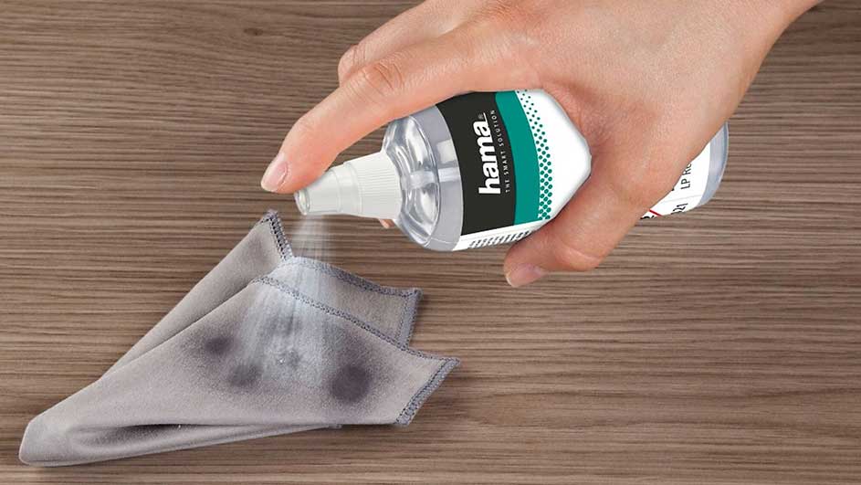 Une main verse du liquide d'une bouteille Hama sur un chiffon gris, le tout sur une surface en bois.