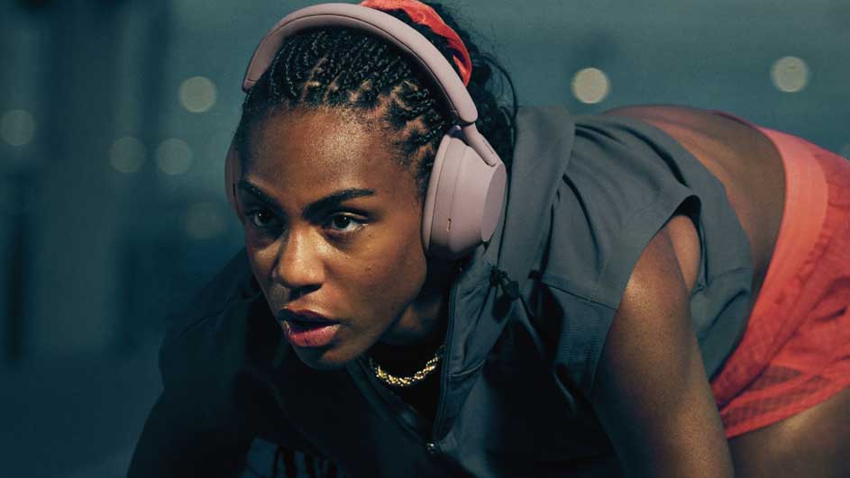 Gros plan d'une personne portant un casque rose et un haut gris, faisant de l'exercice. Le fond est flou avec des lumières.