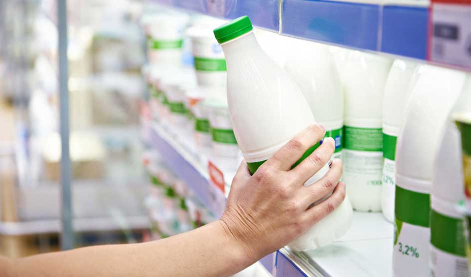 Une main prend une bouteille de lait blanche avec un bouchon vert sur une étagère de magasin.