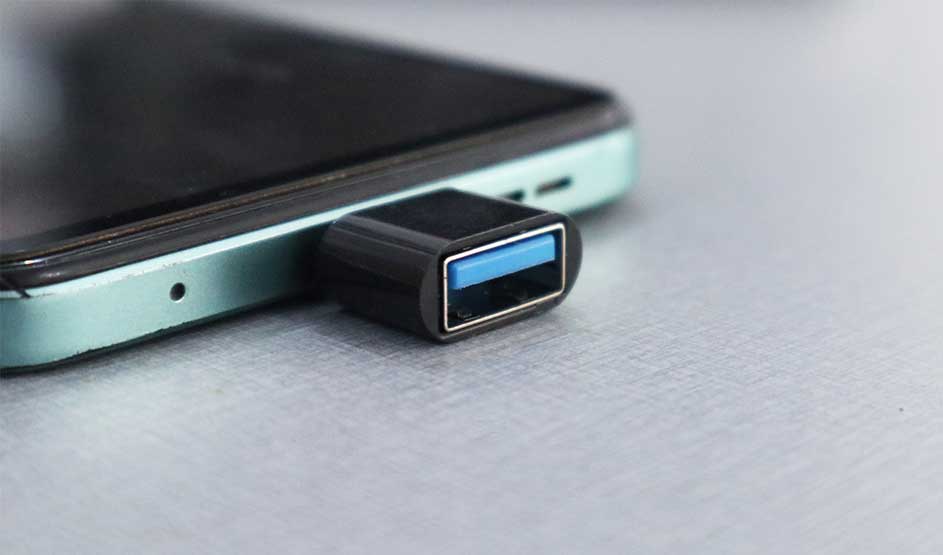 Smartphone au bord vert clair posé sur une table; un petit adaptateur USB noir à insert bleu dépasse de son port de charge.