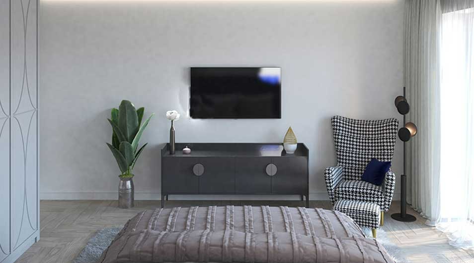 A room with a TV above a gray cabinet, a patterned chair, and a bed in the foreground. Curtains on the right.