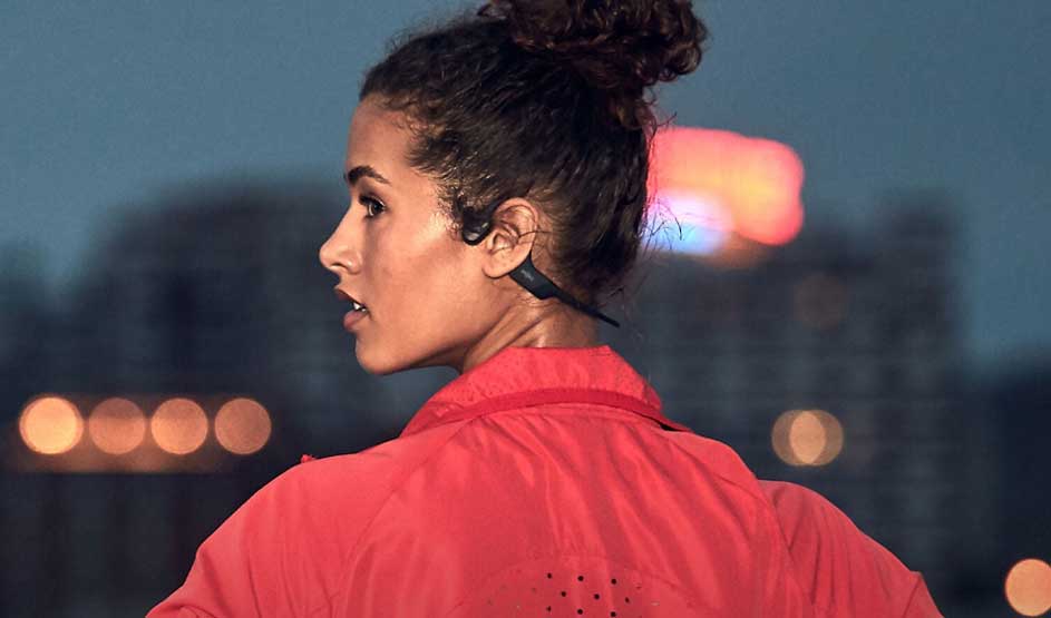 Une femme en veste rouge regarde de côté contre un ciel bleu du soir. Les lumières de la ville s'estompent en arrière-plan. Portrait de profil avec expression sérieuse et coiffure relevée.