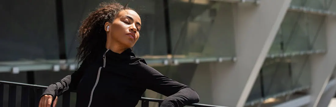A person in a black jacket rests on a railing. A modern building with glass and grey supports is in the background.