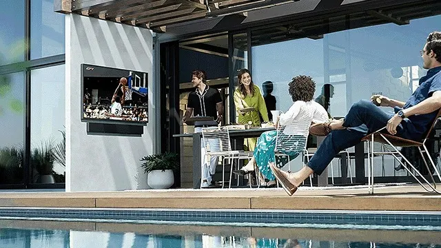 Une télévision diffuse un match de basket-ball près d'une piscine turquoise, avec des meubles de patio.