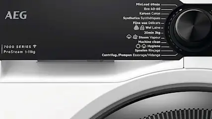 Detail van een AEG wasmachine, met zwarte bedieningspaneel en witte behuizing. Programmakeuzeknop en tekstlabels zichtbaar.