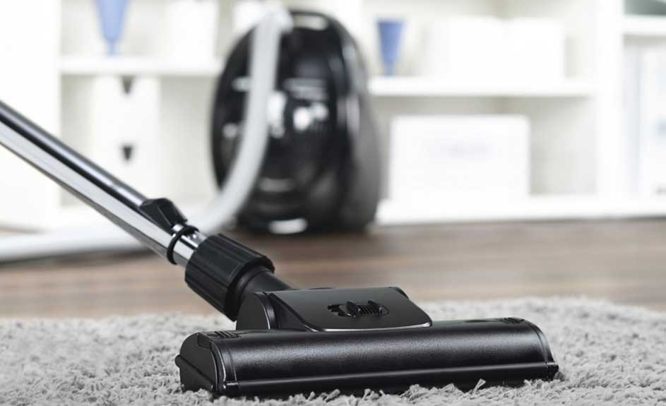 Gros plan d'un aspirateur noir sur un tapis gris, avec un meuble blanc en arrière-plan.