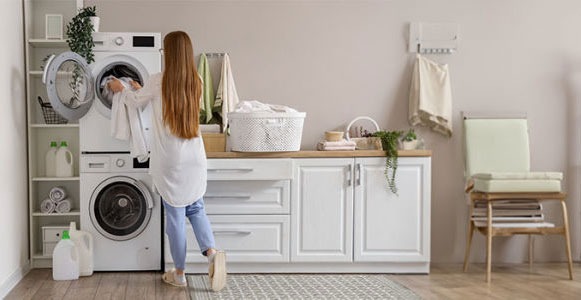 Buanderie avec lave-linge blanc, étagères, armoires et chaise. Un panier à linge est visible.