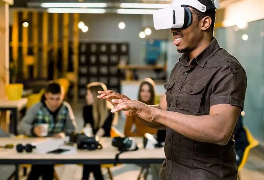 Een man draagt een VR-bril in een kantooromgeving. Op de achtergrond zitten mensen aan bureaus.
